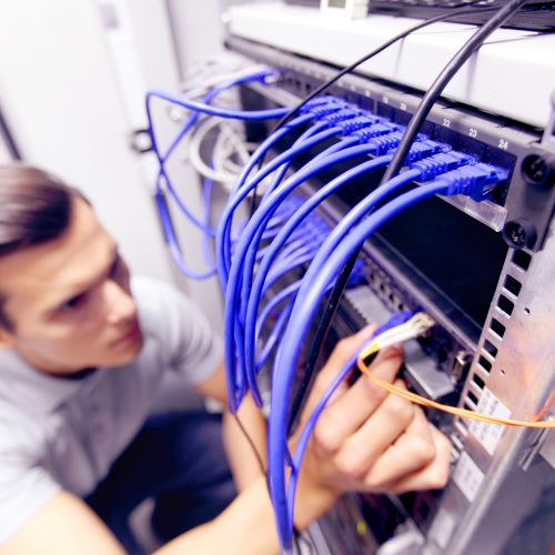 Young engeneer man in network server room connecting wires